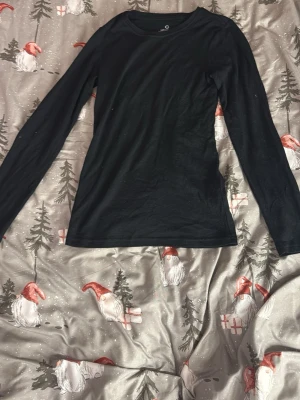 Svart långärmad merinoullstopp XS - En svart långärmad topp från C i 100% merinoull. Enkel och stilren design med rund halsringning och smal passform. Perfekt basplagg för lager på lager under kyliga dagar.