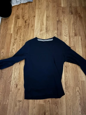 Mörkblå stickad tröja Pier One - En stilren mörkblå stickad tröja från Pier One. Tröjan har rund halsringning med diskreta vita ränder på insidan av kragen och långa ärmar. Perfekt för dig som gillar enkel och klassisk stil.