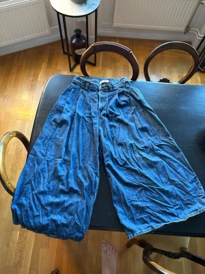 Blå wide jeansbyxor med hög midja - Säljer ett par riktigt vida jeansbyxor i blå denim med hög midja. Byxorna har en loose fit och croppad längd som ger en avslappnad och cool look. Perfekta för dig som gillar statement-plagg och vill ha något bekvämt men ändå stilrent. Klassisk jeansknäppning och fickor fram. 