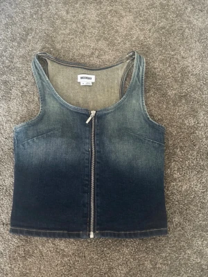 Jeansväst med dragkedja från Weekday - Säljer en snygg jeansväst från Weekday i klassisk blå denim. Västen har en rak passform, breda axelband och en rejäl dragkedja framtill. Perfekt att styla över en t-shirt eller tröja för en cool look.