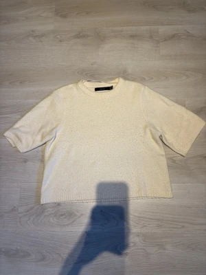 Vit stickad tröja från Vero Moda - En enkel och stilren vit stickad tröja från Vero Moda i storlek M. Tröjan har korta ärmar, rund halsringning och en loose passform. Perfekt att slänga på sig till jeans för en clean look.