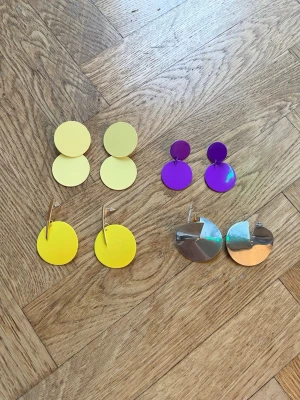 Fyra par statementörhängen i olika färger - Säljer fyra par stora statementörhängen i plast och metall. Ett par är ljusgula med dubbla cirklar, ett par är klargula med guldfärgade detaljer, ett par är lila med dubbla cirklar och ett par är silvriga och snurrade i metall. Perfekta för dig som vill sticka ut!