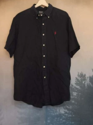 Mörkblå kortärmad skjorta Polo Ralph Lauren - Säljer en mörkblå kortärmad skjorta från Polo Ralph Lauren i storlek L. Skjortan har klassisk krage, vita knappar framtill och den ikoniska röda broderade loggan på bröstet. Tillverkad i 100% linne för en luftig och skön känsla. Pris kan diskuteras, det är altid möjligt att sänka priset!