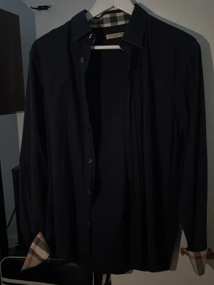 Burberry skjorta  - Säljer en riktigt snygg marinblå skjorta ifrån burberry, säljs eftersom den blivit förliten. Kom privat för fler bilder och funderingar!