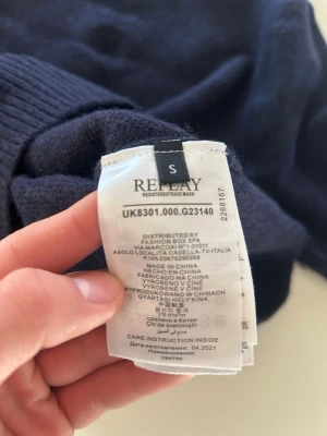 Mörkblå stickad tröja från Replay - Mysig mörkblå stickad tröja från Replay i klassisk modell. Tröjan har rund halsringning, långa ärmar och ribbade muddar vid ärmslut och nederkant. Perfekt för kyliga dagar och enkel att matcha med jeans eller kjol.