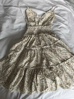 Blommig sommarklänning med volanger - Blommig klänning i ljusa toner med justerbara axelband och v-ringad urringning. Klänningen är stretchig vid midjan och mer utsvängd vid slutet. Köpt i Italien dock så står det ingen märke eller storlek, men den passar XS-M. Skriv via dm vid funderingar 💬🌻