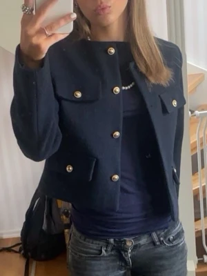 Mörkblå kappa med guldknappar - Säljer en mörkblå kappa  med snygga guldknappar framtill och på fickorna. Jackan har en klassisk, stilren look och är perfekt för dig som vill ha något elegant men ändå chill. Passar till både jeans och kjol.