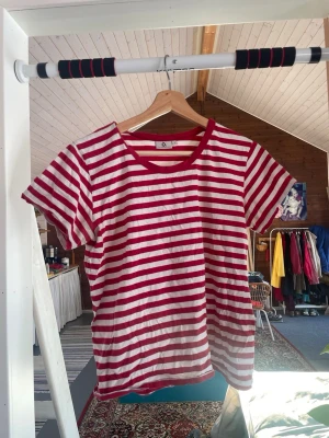 Randig t-shirt från Polarn O. Pyret - Säljer en klassisk t-shirt från Polarn O. Pyret i storlek L. T-shirten har röda och vita horisontella ränder, rund halsringning och korta ärmar. Tillverkad i mjuk bomull. Storlek L.
