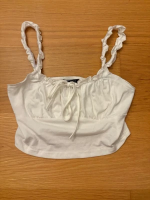 Vit linnetopp med volangband från SHEIN, storlek XS - Supersöt vit linnetopp från SHEIN i storlek XS. Toppen har volangiga axelband och en söt knytning framtill. Perfekt till sommaren och enkel att matcha med jeans eller kjol. Gjord i mjuk bomull för en skön känsla. 62% Polyester, 4% Elastan, 34% Bomull.