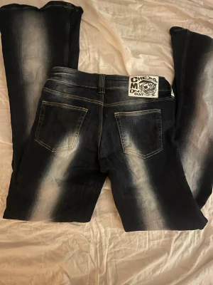 Svarta jeans med vit tvätt och tryck - Säljer ett par mörkblå Cheap Monday jeans med vit tvättad effekt längs benen och bakfickorna. Klassisk femficksmodell med ett stort vitt Cheap Monday-märke med döskalle på bakfickan. Jeansen har raka ben och är gjorda i jeansmaterial. Storlek 28/32💕