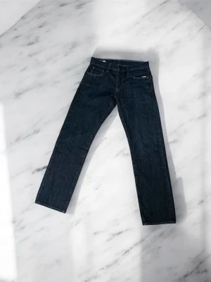 Mörkblå G-star jeans - Mörkblå G-star jeans med klassisk femficksdesign och raka ben. Jeansen har snygga kontrastsömmar och subtil broderad detalj på bakfickorna. Passformen är loose och materialet är slitstarkt jeans. Perfekt för dig som gillar en avslappnad stil. Storleken är W30 L32. Jeansen är helt oanvända. Skriv om du undrar över något. Kan gå ner i pris vid snabb affär. Nypris 1300kr