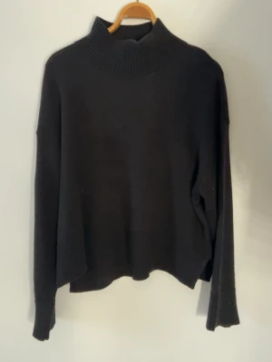 Svart polotröja med ribbad krage - Svart polotröja med bred, ribbad krage och långa ärmar. Tröjan har en loose passform och är stickad i mjukt material som passar perfekt när det är kyligt ute. Storlek XL men sitter som M/L