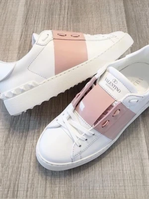 Valentino Garavani sneakers med rosa detalj - Säljer ett par snygga Valentino Garavani sneakers i vitt skinn med bred rosa rem över vristen och coola nitar på hälen. Skorna har klassisk snörning och chunky vit sula med mönstrad undersida. Perfekta för dig som vill sticka ut med en lyxig touch.
