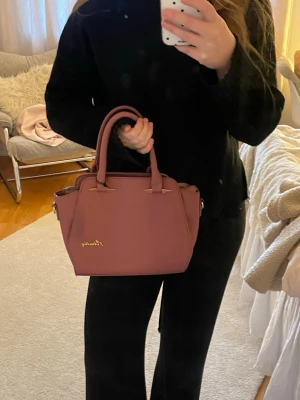 Rosa handväska från Alimathy - Säljer en snygg rosa handväska från Alimathy med guldfärgade detaljer och många fack! 