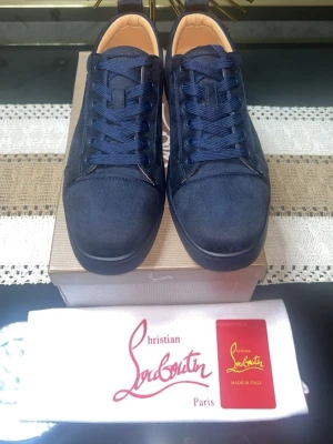 Mörkblå sneakers från Christian Louboutin - Snygga mörkblå sneakers från Christian Louboutin i mocka med klassisk röd sula och rund tå. Skorna har matchande mörkblå snörning och diskret broderad logga på hälen. Insidan är i beige läder för extra lyxig känsla.