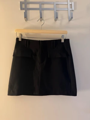Svart kortkjol med fickdetaljer - Säljer en skit snygg svart kostym kjol med fickor som detaljer där fram. Denna är från gina tricot och varit slut såld rätt länge. Säljer denna då den inte kommer till användning 