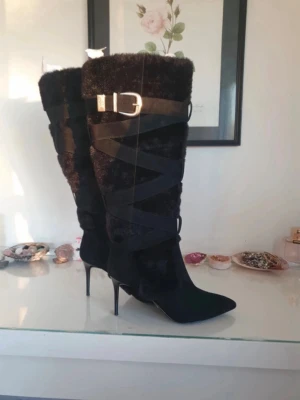 Svarta höga boots från Steve Madden - Säljer ett par svarta höga boots från Steve Madden med spetsig tå och smal hög klack. Skorna har pälsimitation, dekorativa band runt skaftet och ett snyggt spänne i guld. Perfekta för dig som vill sticka ut med en lyxig och trendig look. Skorna är helt nya och köpta på Zalando så dem är äkta. Dem går för 2400kr men jag lägger ut dem för 2000kr då jag bara vill få dem sålda. Är storlek 40 och sitter som en 40