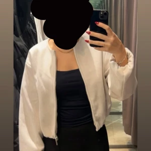 Beige bomberjacka med dragkedja - Säljer en beige bomberjacka med rund halsringning och två fickor framtill. Jackan har en clean look utan synliga detaljer och stängs med dragkedja. Modellen är lite loose och har långa ärmar med lätt puffig känsla. Perfekt för dig som gillar minimalistisk stil.