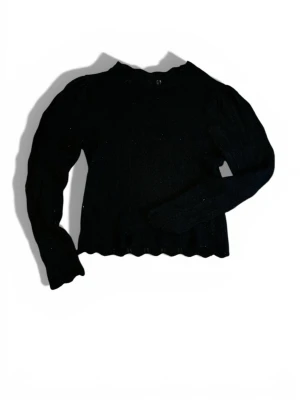 Svart stickad tröja med vågig kant och mönstrat ihåligt material - Säljer en svart stickad tröja med lång ärm och vågig kant nertill. Tröjan har ett ihåligt mönster som ger en snygg detalj.