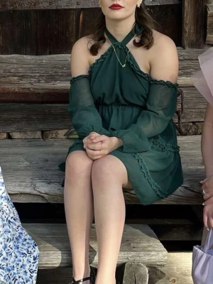 Mörkgrön kort klänning med volang - Supersöt mörkgrön kort klänning med halterneck och offshoulder ärmar i transparent tyg. Klänningen har volangdetaljer och en flowy kjol, perfekt för dig som vill sticka ut. Materialet känns lätt och luftigt, och modellen har en snygg v-ringning och markerad midja.