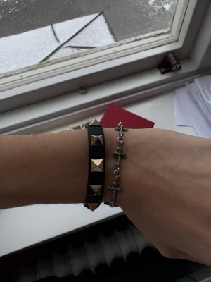 Valentino svart läderarmband med nitar - Säljer ett svart armband från Valentino. Armbandet har justerbart spänne och kommer med originalpåse och box. Den har öppnat sig lite i kanten men inget som syns, därav priset.