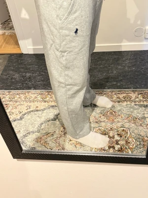 Grå mjukisbyxor från Polo Ralph Lauren - Säljer ett par ljusgrå mjukisbyxor från Polo Ralph Lauren med klassisk blå logga broderad på vänster ben. Byxorna har dragsko i midjan, raka ben och är gjorda i mjuk bomull. Perfekta för chill dagar eller när du vill vara bekväm. straight leg
