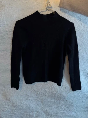 Svart stickad polotröja - En super snygg enkel och stilren svart stickad polotröja med lång ärm. Tröjan har en hög hals och är gjord i mjukt material som passar perfekt till kyligare dagar. 