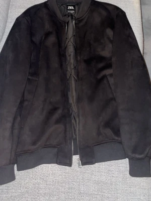 Svart mocka bomberjacka - Säljer en svart bomberjacka från Zara i mjuk mocka. Jackan har klassisk bomberkrage, muddar vid ärmslut och nederkant samt dragkedja framtill. Enkel och stilren design som passar till det mesta.