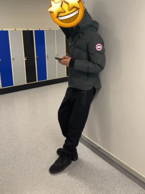 Svart pufferjacka från Canada Goose - Säljer en svart pufferjacka från Canada Goose med huva och klassisk logga på ärmen. Jackan har dragkedja, stora fickor framtill och ribbade muddar vid ärmsluten. Perfekt för kalla dagar och riktigt snygg streetstil.