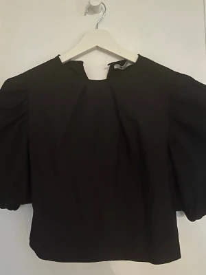 Svart blus från Na-kd - Säljer en svart blus med breda puffärmar och rund halsringning. Toppen har en stilren och enkel design. Strolek 36 i nyskick💕