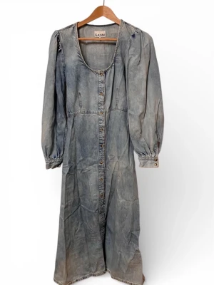 Lång jeansklänning från Ganni - Säljer en långärmad jeansklänning från Ganni i tvättad indigo. Klänningen har knappar hela vägen framtill, rundad halsringning och lätt puffade axlar. Perfekt för dig som gillar en avslappnad men ändå snygg look.