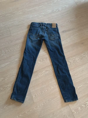 Replay Hyperflex blå jeans - Säljer ett par Replay Hyperflex jeans i klassisk blå tvätt. Jeansen har fem fickor, normal passform och raka ben. Materialet är stretchigt jeans för extra komfort och rörelsefrihet. Snygga detaljer med Replay-logga på fickan och läderpatch bak i midjan.