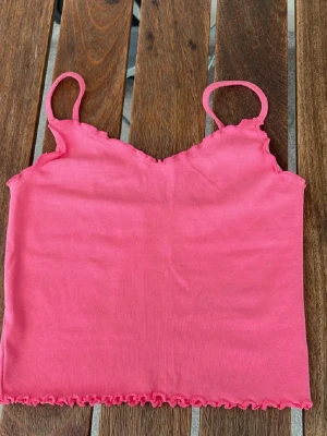 Rosa armlös topp med volangdetalj  - Säljer min tyvärr för liten söt rosa topp, lappen är dock bortklippt så vet inte exakt storleken men gissar xs-s💕toppen är ganska croppad💕det går inte att justera axelbanden💕perfekt för sommarn eller som ett lager under en kofta💕