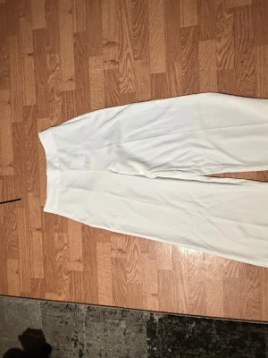 Vita vida byxor i storlek S - Säljer ett par fräscha vita byxor i storlek S. Byxorna har en rak och vid passform med hög midja och är tillverkade i ett mjukt tyg som känns skönt mot huden. Perfekta för en clean och stilren look.