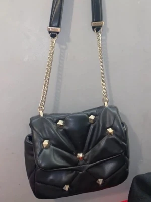 Svart axelväska med nitar från Zara - Ni kan även köpa fler saker o mötas upp för en billigare ”paket pris” då de blir lättare än att frakta.                    Cool svart axelväska från Zara i skinnimitation med quiltad design och guldiga kedjedetaljer. Väskan har snygga guldfärgade nitar på locket och kan bäras både med kedja eller axelrem. Perfekt storlek för det viktigaste och ger en edgy vibe till din outfit.