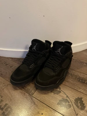 Jordan 4 black cats - Säljer ett par helsvarta Nike Air Jordan 4 sneakers med klassisk Jumpman-logga på plösen och hälen. Skorna har snörning, meshdetaljer och en robust sula. Materialet är en mix av mocka och syntet, vilket ger en clean och stilren look. Pris kan diskuteras vid snabbaffär. 