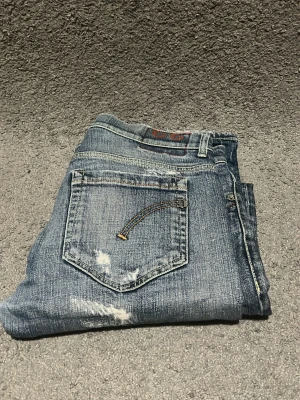 Dondup George - Säljer ett par blå skinny jeans med coola slitningar och slitna detaljer på både fram- och baksida. Jeansen har klassisk femficksdesign, låg midja och kontrastsömmar på bakfickorna. Perfekta för dig som gillar en avslappnad och trendig look. W 43cm L 103cm