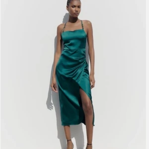 Grön långklänning från Zara i S. - Säljer en smaragdgrön långklänning från Zara med tunna axelband och snygg omlott-detalj framtill. Klänningen har en slits och är tillverkad i ett glansigt, mjukt material som ger en lyxig känsla. Perfekt för dig som vill sticka ut lite extra. Använd men är fortfarande i gott skick. 