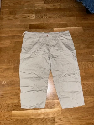 Beiga croppade byxor Feeling Woman - Snygga beiga croppade byxor från Feeling Woman. Byxorna har normal passform, raka ben och klassisk knappstängning framtill. Tillverkade i mjukt bomullsmaterial som känns skönt mot huden. Perfekta för en avslappnad och stilren look.