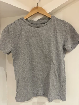 Grå basic t-shirt från 157 XS - Enkel grå t-shirt från 157 i storlek XS. Tillverkad i mjuk bomullsblandning med 90% bomull och 10% viskos. Klassisk passform med rund hals och korta ärmar, perfekt till jeans eller shorts.