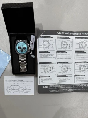 Turkos kronografklocka från OLEVS - Snygg kronografklocka från OLEVS med turkos urtavla och tre svarta subdials. Klockan har en robust länkarmband i silverfärgad metall och detaljerade knappar på sidan. Modern design med datumvisning och markerade index. Perfekt accessoar för dig som vill sticka ut.