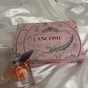 Lancome parfym med presentask - Snygg parfym från Lancome med rosa presentask. Perfekt för dig som vill ha något extra på hyllan eller ge bort som present. Flaskans design är stilren och modern. Volym och ingredienser framgår ej på bilderna.