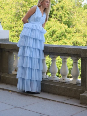 Ljusblå volangklänning med v-ringning - Säljer en drömmig ljusblå långklänning med flera lager volanger och v-ringad överdel. Klänningen är ärmlös och har en markerad midja som ger en elegant siluett. Perfekt för speciella tillfällen och sommarens fester. Perfekt balklänning!