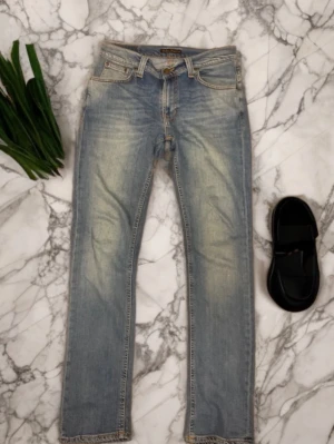 Nudie Jeans 31/32 - Säljer ett par Nudie jeans i storlek 31/32. Klassisk ljusblå denim med lätt slitning/washed effekt framtill och baktill (original från märket, ej egen slitage). Raka ben och normal midja. Jeansen är i mycket bra skick utan fläckar eller hål. Kvalitativ och mjuk denim som sitter snyggt.  Perfekta både till vardag och mer dressade outfits. Endast sparsamt använda.  Skick: Mycket bra Märke: Nudie Jeans Storlek: 31/32