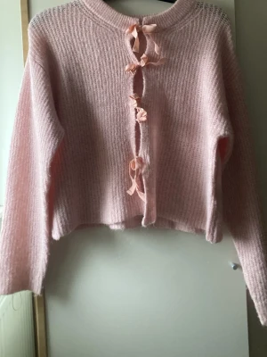 Rosa stickad kofta med knyt från Gina Tricot - Supersöt rosa stickad kofta från Gina Tricot med långa ärmar och fina knytband framtill. Koftan har en croppad passform och är perfekt för dig som gillar mjuka och mysiga plagg med en gullig twist.