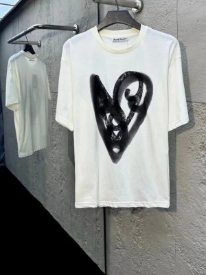 Vit t-shirt med svart hjärta Acne Studios - Vit t-shirt från Acne Studios i bomull och hampa, med ett stort svart hjärta tryckt framtill. Klassisk passform och rund halsringning. Perfekt för dig som gillar streetstyle och vill sticka ut med en unik print.