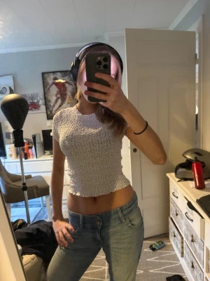 Vit croppad topp från Gina Tricot - Säljer en vit croppad topp från Gina Tricot i storlek S. Toppen har korta ärmar och är gjord i ett ribbat, stretchigt material med snyggt rynkad struktur. Perfekt till jeans eller kjol för en chill och trendig look.