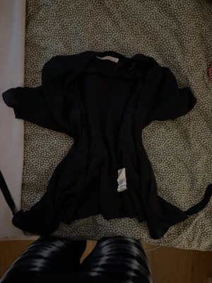 Svart omlottjacka från Zara Trafaluc - Svart omlottjacka från Zara Trafaluc Collection i tunn, flowy polyester. Jackan har knytband i midjan och ett stilrent, enkelt snitt som ger en chill och snygg vibe. Perfekt att slänga över en outfit för extra edge.