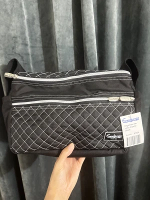 Svart quiltad organiser från Emmaljunga helt ny  - Svart organiser-väska från Emmaljunga med snyggt quiltat mönster och vita kontrastsömmar. Väskan har flera dragkedjefack och bred axelrem. Perfekt för att hålla koll på småprylar och accessoarer. Tillverkad i slitstark polyester.