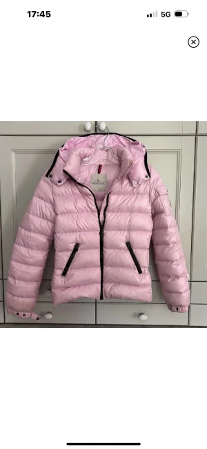 Ljusrosa dunjacka från Moncler - Superfin ljusrosa dunjacka från Moncler med svart dragkedja och svarta detaljer vid fickorna. Storlek 12 i barnstorlek men skulle säga att den passar en XS/S🥰 Lite smuts på inre armar och färre defekter men inget större märkvärdigt🫶🏼🫶🏼
